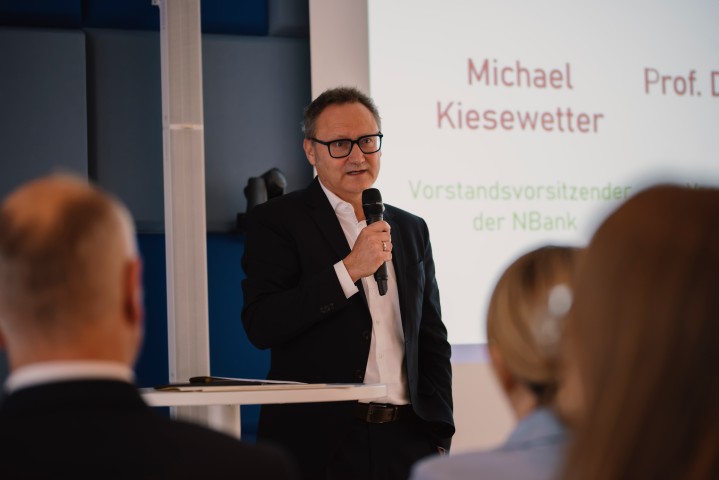 Michael Kiesewetter, Vorstandsvorsitzender der NBank, steht an einem Rednerpult und spricht mit einem Mikrofon vor Publikum.
