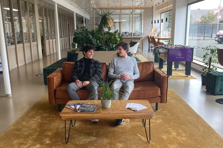 Die Auszubildenden im IT-Ausbildungsverbund Fouad und Max sitzen auf einem roten Sofa und unterhalten sich