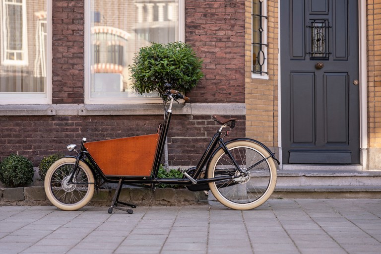 Typisches holländisches Lastenfahrrad, das vor einem Haus geparkt ist.